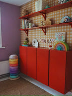 Papier peint Vichy jaune ocre d'Atelier Chien derrière une armoire rouge et des étagères murales.