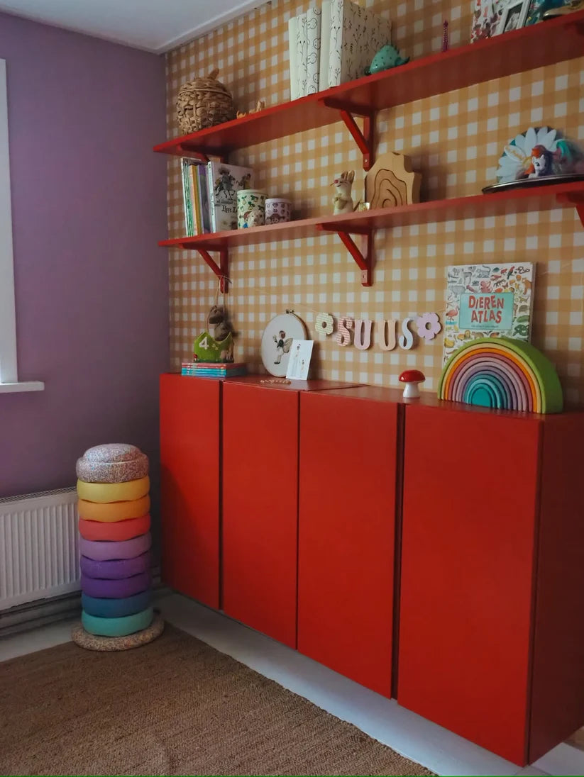 Papier peint Vichy jaune ocre d'Atelier Chien derrière une armoire rouge et des étagères murales.
